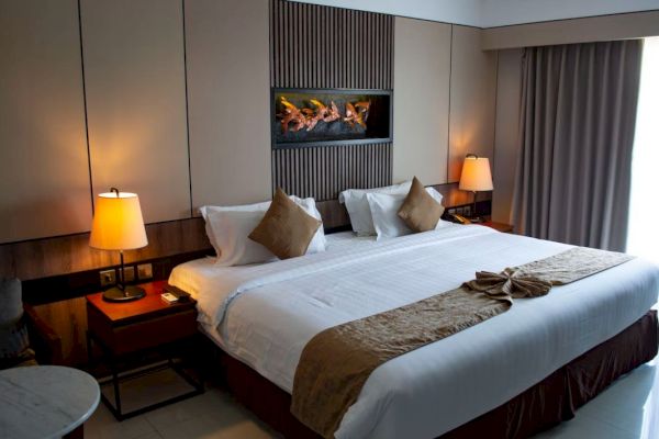 This image shows a neatly made hotel bed with two lamps on either side, a modern wall feature, and a curtained window, creating a cozy ambiance.