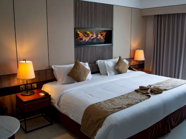 This image shows a neatly made hotel bed with two lamps on either side, a modern wall feature, and a curtained window, creating a cozy ambiance.