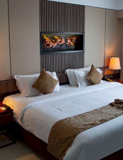 A well-lit hotel room with a king-sized bed, lamps on each side, a piece of art on the wall, and a large window with curtains.