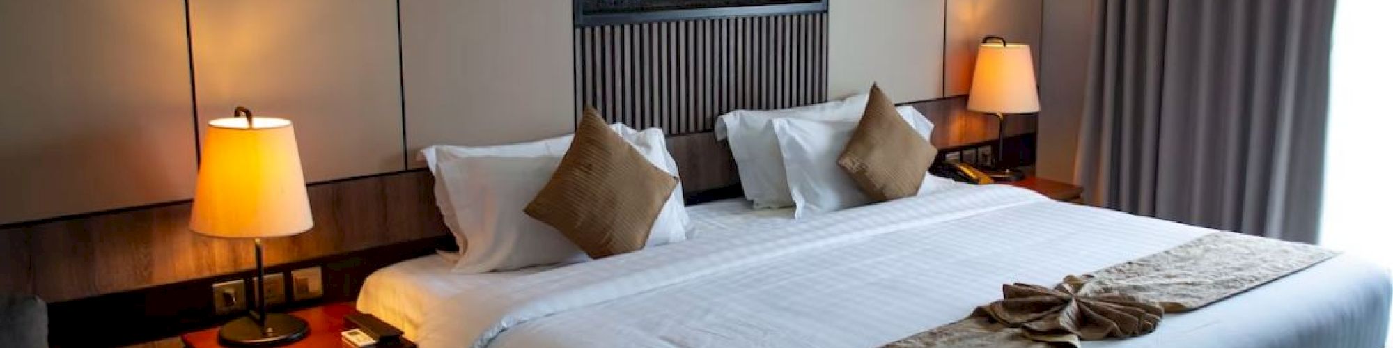 A cozy hotel room with a large bed, decorative pillows, bedside tables with lamps, and a wall decoration above the headboard.