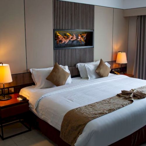 A neatly arranged hotel bedroom features a large bed with pillows, two bedside lamps, and a modern wall decoration, ending the sentence.
