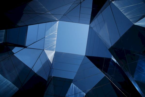 This image shows a geometric pattern formed by the reflective surfaces of modern glass architecture, creating an abstract view of the sky.