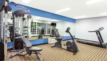 This image shows a modern gym with exercise equipment, including a weight machine, stationary bike, and treadmill, with large mirrors on the wall.