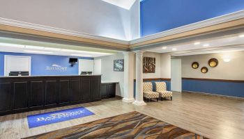 The image shows a hotel lobby area with a reception desk, chairs, and wall decor. The setting is clean and modern with blue and neutral tones.