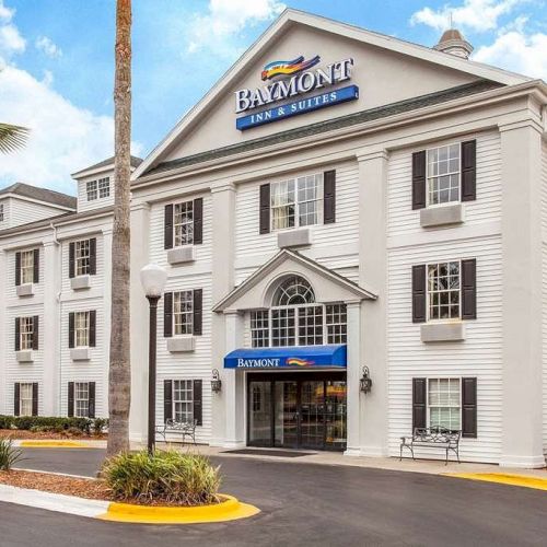 The image shows the front of a Baymont Inn & Suites hotel building with a well-maintained exterior and a few palm trees.