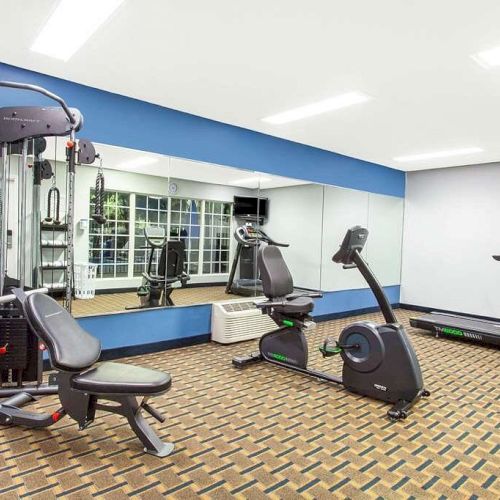 A small gym features a multi-station machine, a stationary bike, and a treadmill with a large mirror reflecting the equipment, ending the sentence.