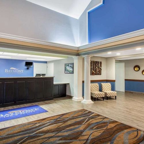 This image shows a hotel lobby with a reception desk, two chairs, decorative wall hangings, and a rug on the floor.