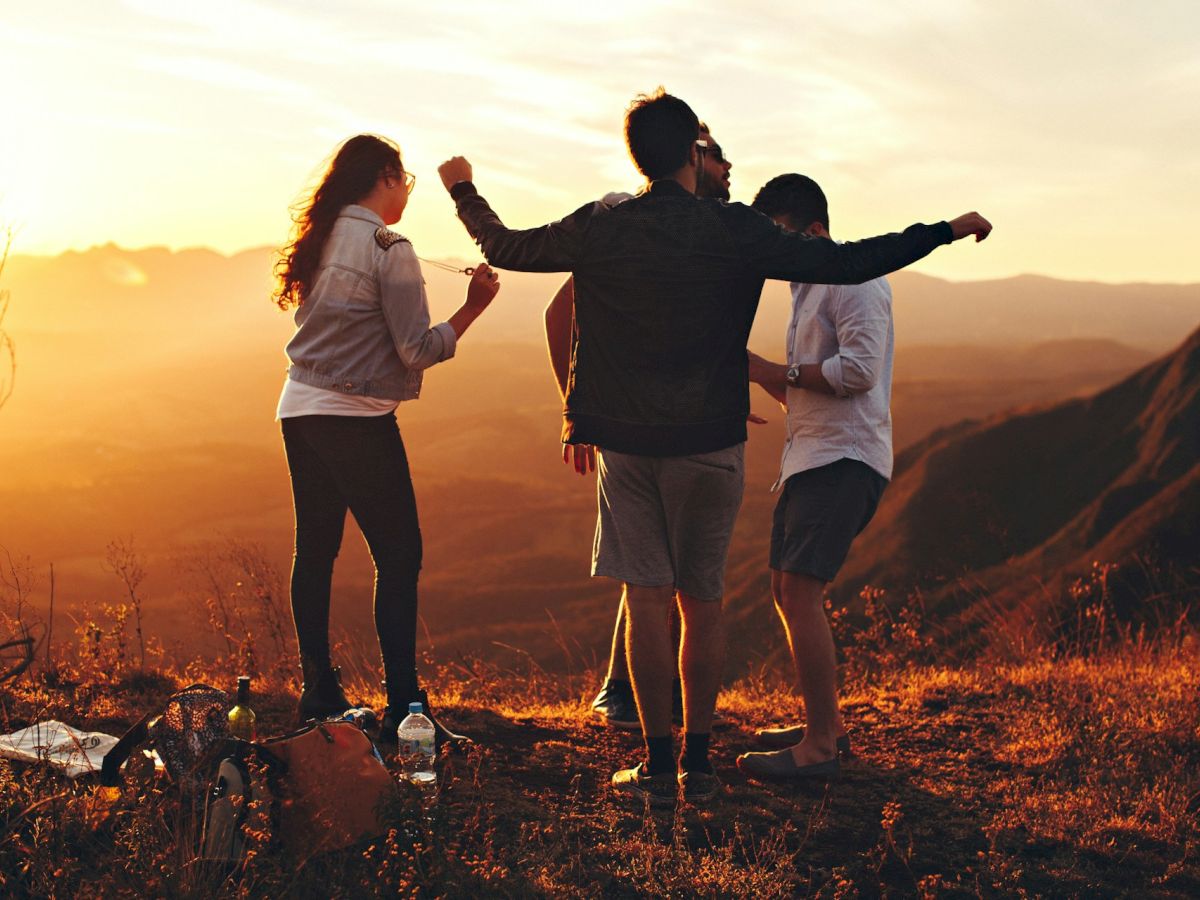 Four people are enjoying an outdoor moment during sunset; three males and one female standing and conversing on a hill or mountain area.