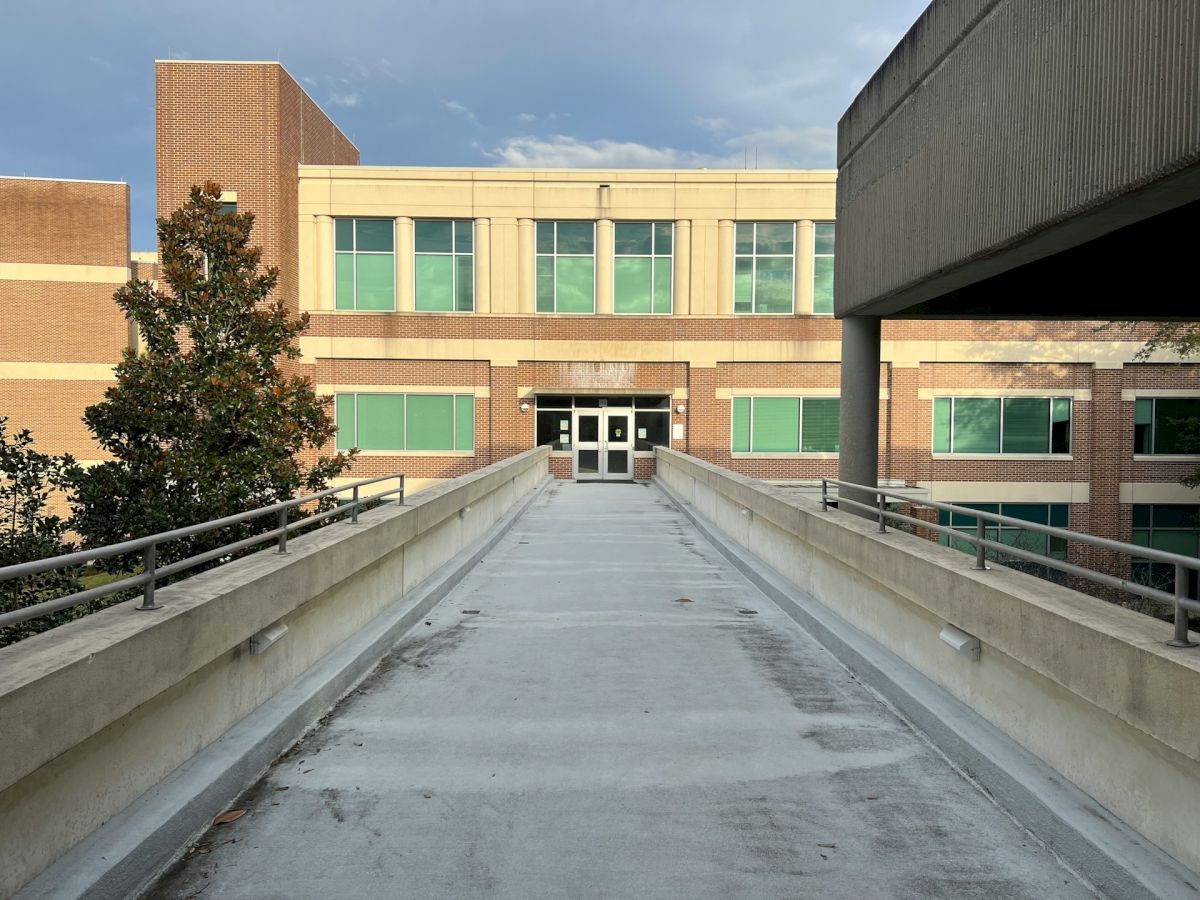 A brick building with green windows and a walkway leading to the entrance is visible, with overcast skies above.