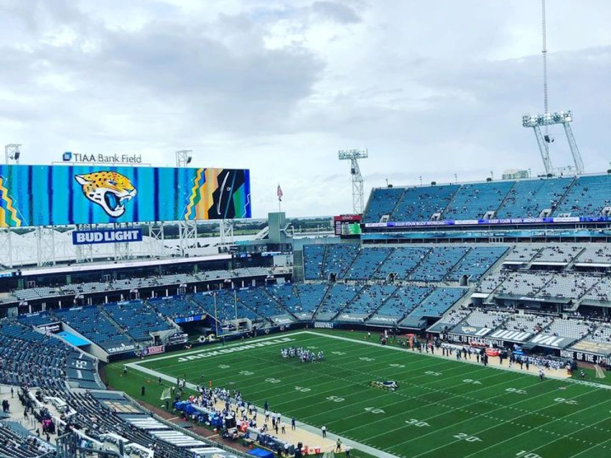 This image shows an empty football stadium with a large screen displaying the Jacksonville Jaguars' logo, under a cloudy sky.