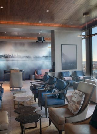 A modern lounge with several chairs and tables, overlooking a scenic view with a Ferris wheel and waterfront through large windows.