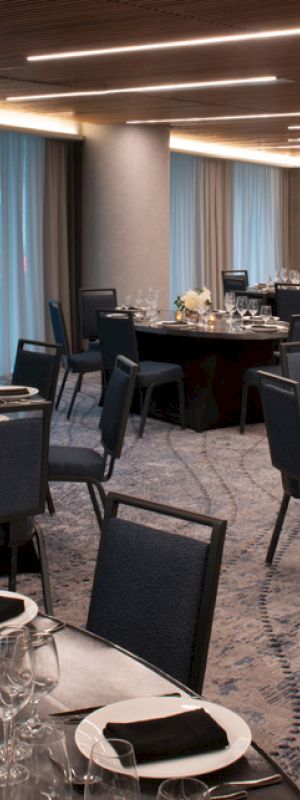 The image shows a banquet hall setup with round tables, elegant place settings, and chairs. The room is well-lit with modern lighting fixtures.
