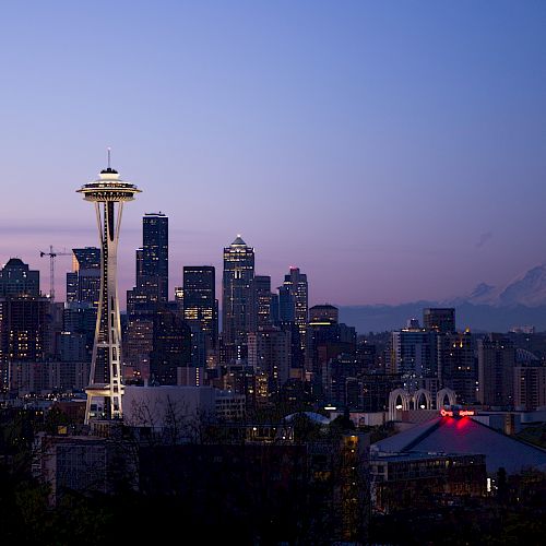 This image shows the Seattle skyline at twilight, featuring the iconic Space Needle and Mount Rainier in the background.